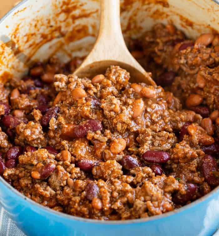 A wooden spoon scooping up chili from a cooking pot.