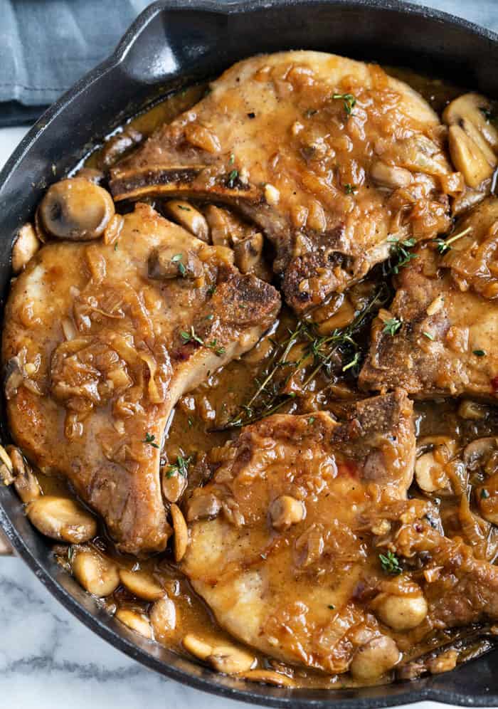 Pork Chops in a cast iron skillet smothered with a french onion sauce with mushrooms and gravy.