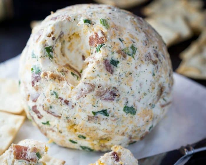 A bacon ranch cheddar cheese ball with crackers around it.