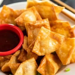 Crab Rangoon on a plate with sweet and sour sauce on the side.