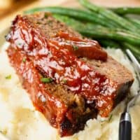 Cracker Barrel Meatloaf with glaze topped with ketchup sauce on top of mashed potatoes.