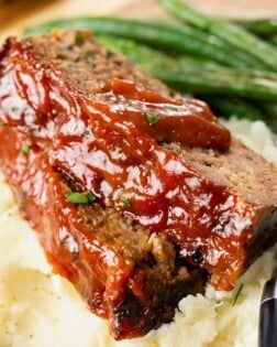 Cracker Barrel Meatloaf with glaze topped with ketchup sauce on top of mashed potatoes.