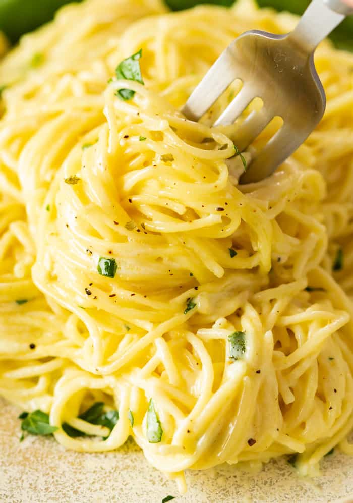 A close up view of buttery noodles in a creamy lemon sauce with a fork in them and fresh parsley on top.