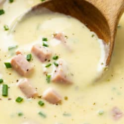 A wooden spoon scooping up creamy ham and potato soup topped with chives.