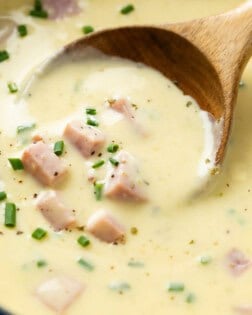 A wooden spoon scooping up creamy ham and potato soup topped with chives.