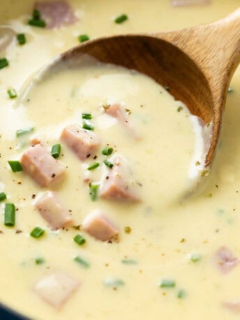 A wooden spoon scooping up creamy ham and potato soup topped with chives.