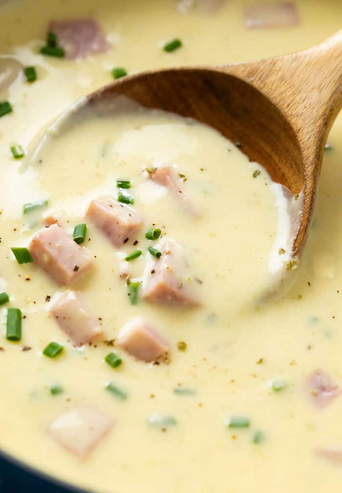 A wooden spoon scooping up creamy ham and potato soup topped with chives.