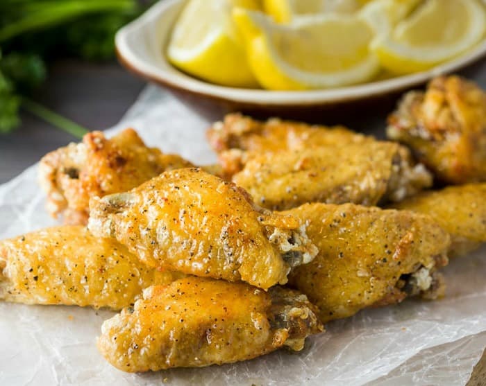 A pile of lemon pepper wings on a white napkin with lemon wedges in the background.