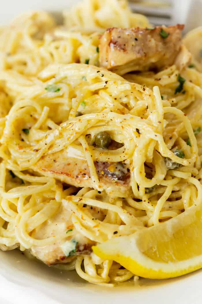 A close up view of angel hair pasta in a creamy Caesar sauce with grilled chicken, capers, and lemons.