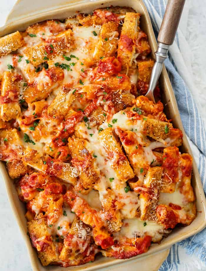 A casserole dish filled with Chicken Parmesan Casserole with a spoon inserted into it.