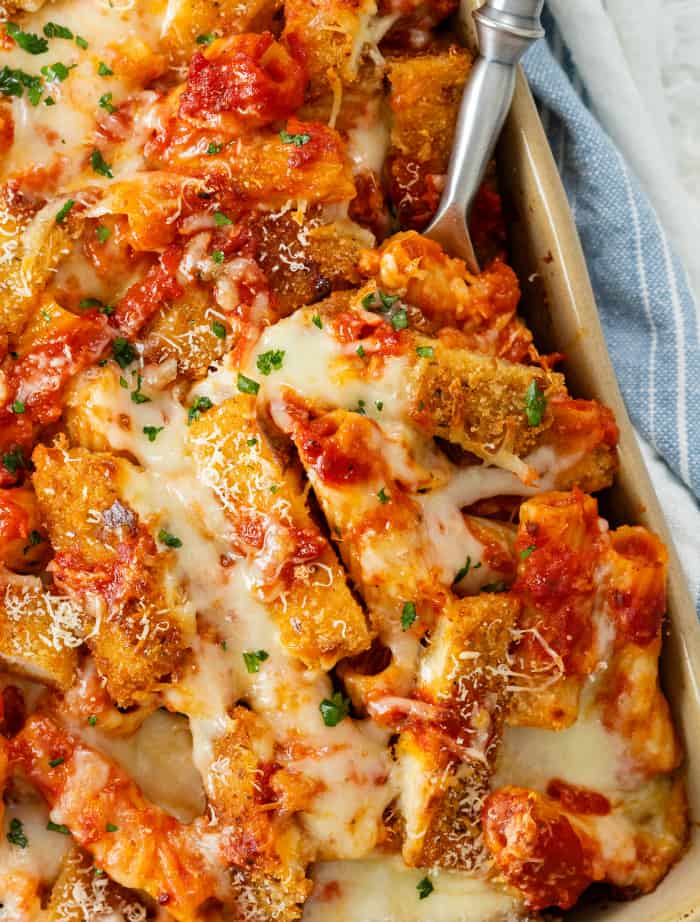 A spoon in a casserole dish scooping up chicken Parmesan casserole