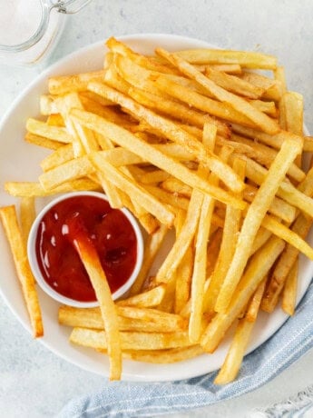 A white plate full of homemade McDonald's French Fries and kechup.