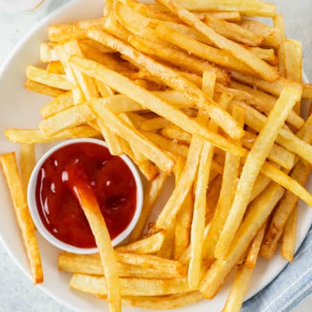 A white plate full of homemade McDonald's French Fries and kechup.