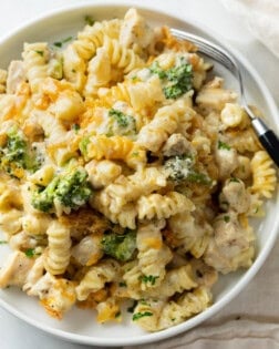 A white plate with Chicken Noodle Casserole with with a creamy mushroom cheese sauce and broccoli.