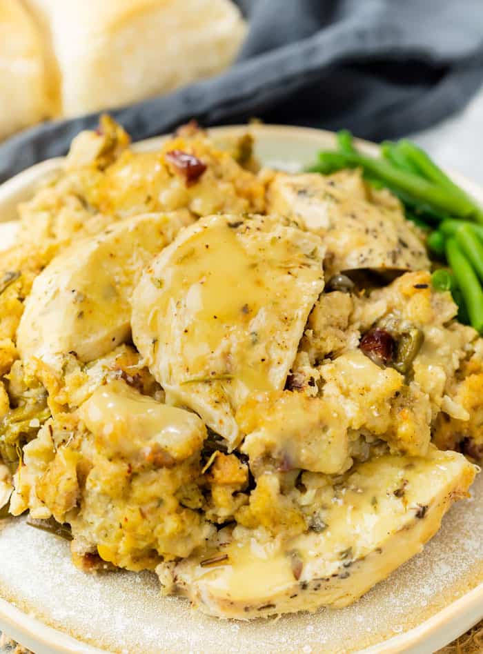 A plate piled with stuffing and chicken with gravy drizzled on top and green beans in the background.