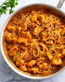 Chicken Scallopini in a skillet with red sauce, spaghetti, and chicken.