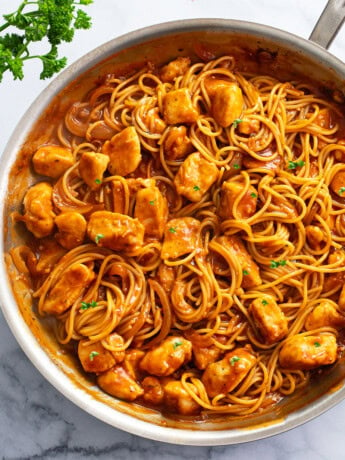 Chicken Scallopini in a skillet with red sauce, spaghetti, and chicken.