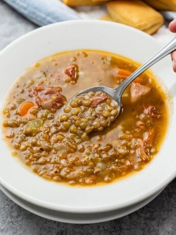 A white bowl full of lentil soup with ham and spoon scooping it up.
