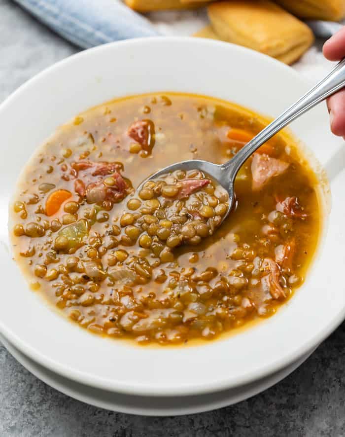 A white bowl full of lentil soup with ham and spoon scooping it up.