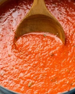 A wooden spoon scooping up homemade marinara sauce from a pot.