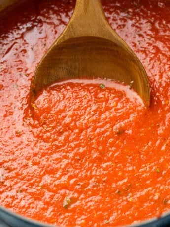 A wooden spoon scooping up homemade marinara sauce from a pot.
