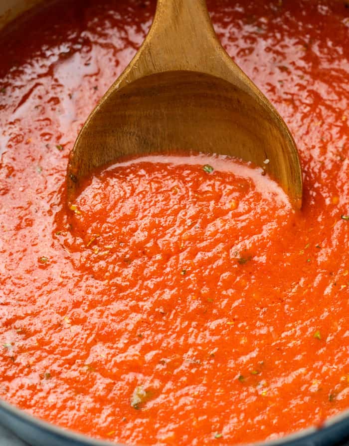 A wooden spoon scooping up homemade marinara sauce from a pot.