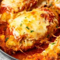 A breaded chicken breast topped with melted mozzarella in a pan with marinara sauce for Baked Chicken Parmesan.