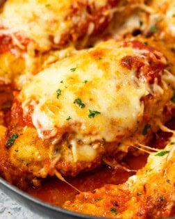 A breaded chicken breast topped with melted mozzarella in a pan with marinara sauce for Baked Chicken Parmesan.