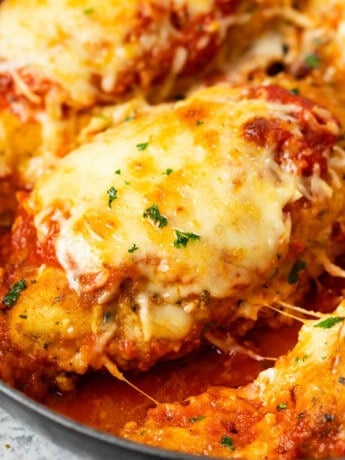 A breaded chicken breast topped with melted mozzarella in a pan with marinara sauce for Baked Chicken Parmesan.