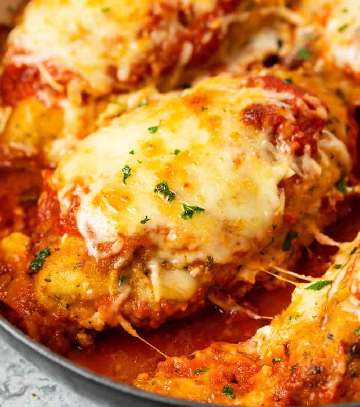 A breaded chicken breast topped with melted mozzarella in a pan with marinara sauce for Baked Chicken Parmesan.