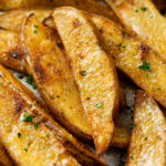 A pile of baked potato wedges with chopped parsley on top.
