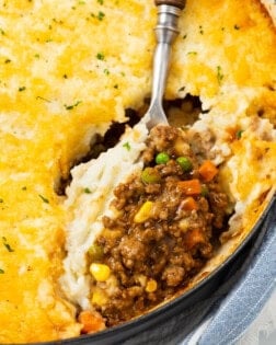 A large spoon scooping Shepherds Pie from a casserole dish.