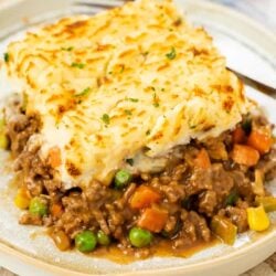 A plate with a slice of easy shepherds pie with ground beef with a fork in the background.