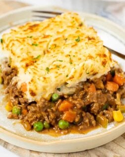 A plate with a slice of easy shepherds pie with ground beef with a fork in the background.