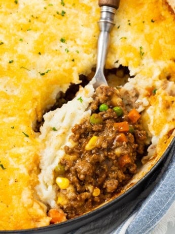 A large spoon scooping Shepherds Pie from a casserole dish.