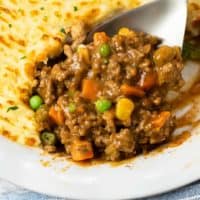 A spoon scooping up ground beef filling out of a dish of Sheperd's Pie