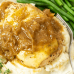 Chicken Breasts topped with melted mozzarella and a French Onion Sauce on top of mashed potatoes with green beans in the background.