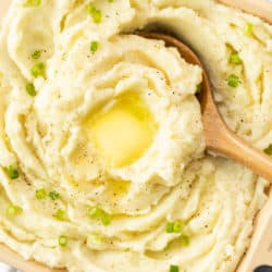Swirls of mashed potatoes in a serving dish topped with melted butter and green onions.