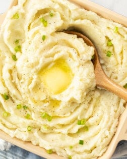 Swirls of mashed potatoes in a serving dish topped with melted butter and green onions.