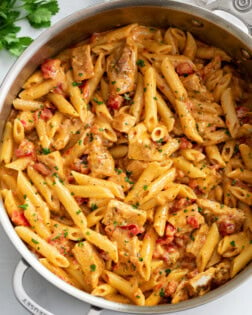 Cajun Chicken Pasta in a skillet with penne pasta, cream sauce, and tomatoes.