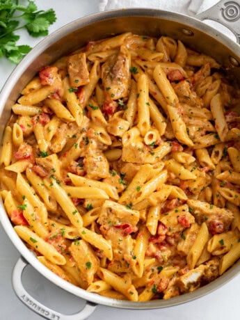 Cajun Chicken Pasta in a skillet with penne pasta, cream sauce, and tomatoes.