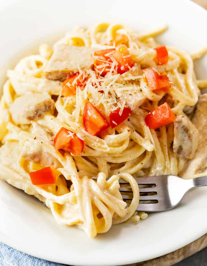 A white plate with a fork with Cajun Chicken Pasta topped with diced tomatoes and shredded Parmesan cheese.