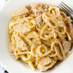 A white bowl filled with Cajun Chicken Pasta with fettuccine noodles and Alfredo sauce.