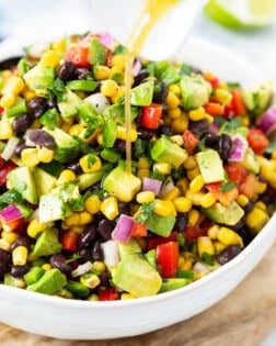 A white bowl filled with cowboy caviar with dressing being drizzled on top.