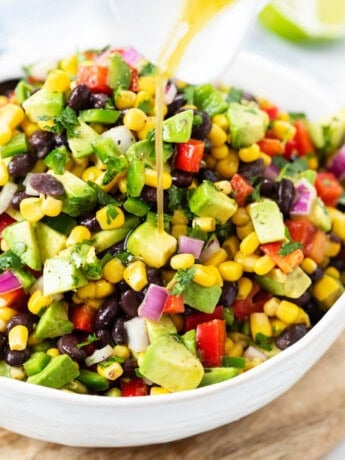 A white bowl filled with cowboy caviar with dressing being drizzled on top.