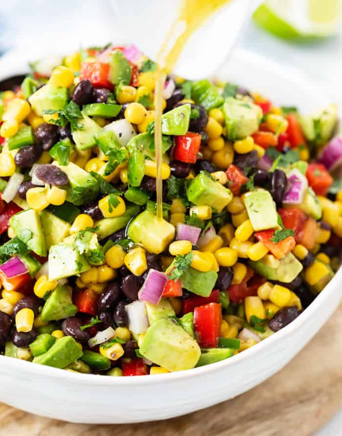 A white bowl filled with cowboy caviar with dressing being drizzled on top.