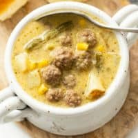 A white crock filled with creamy hamburger soup with a spoon in it.