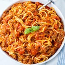 A white bowl filled with Instant Pot Spaghetti with marinara sauce and ground beef, topped with fresh basil.
