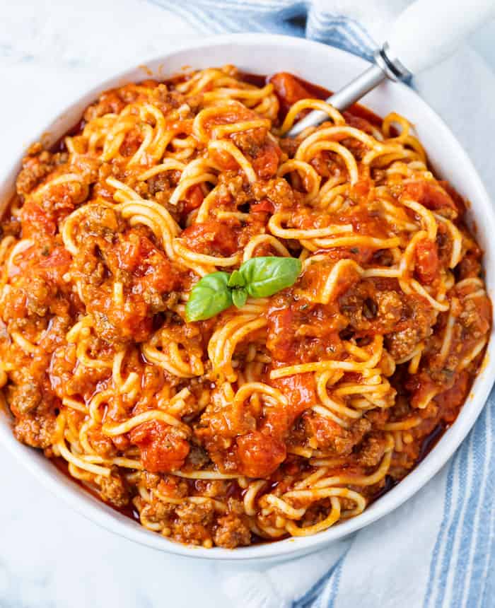 A big white bowl full of Instant Pot Spaghetti with a basil leaf in the middle