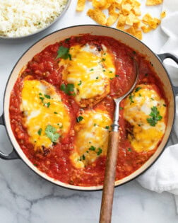 A skillet filled with Salsa Chicken topped with cheese and cilantro with a spoon in it.